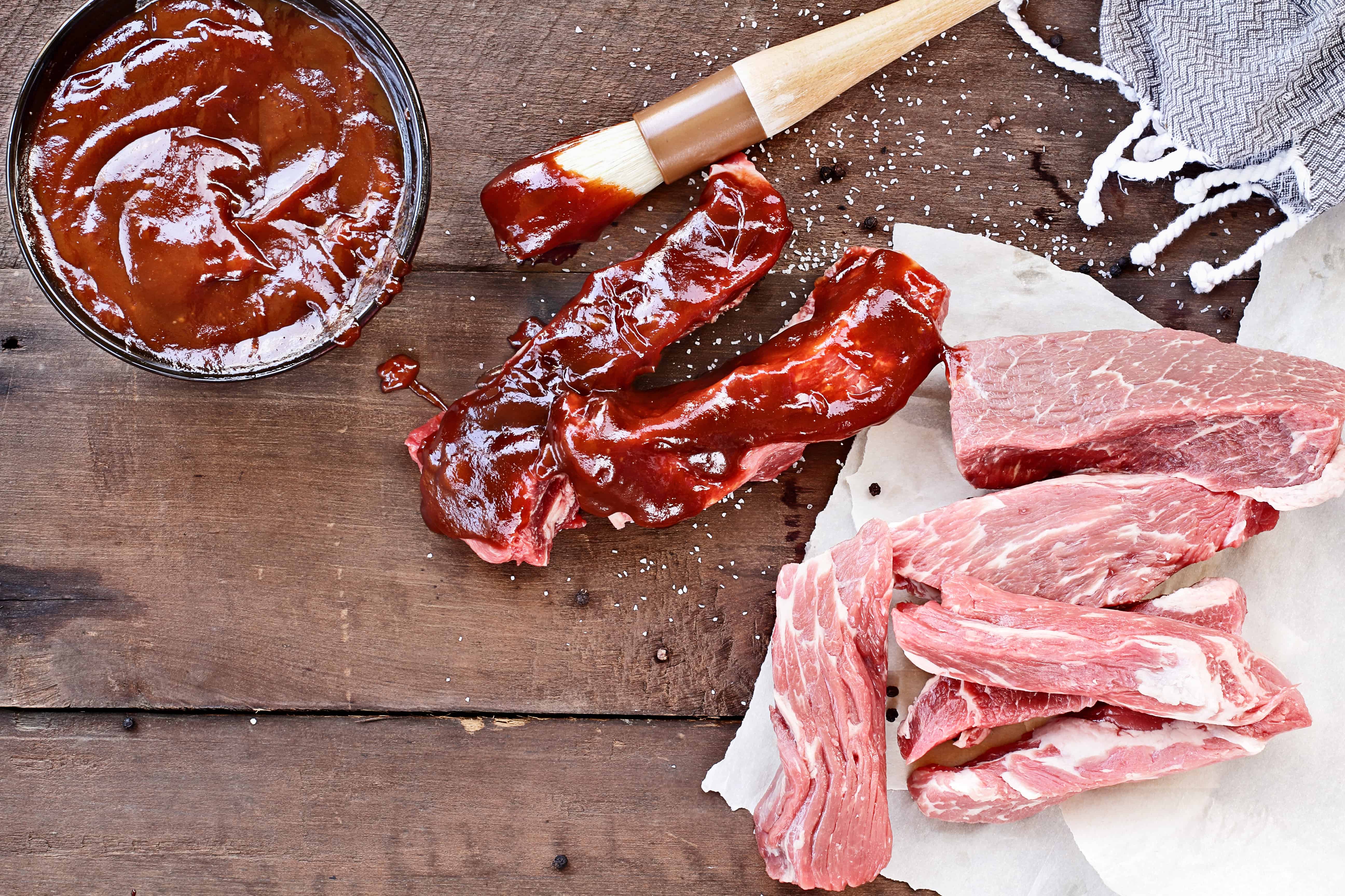 Country ribs with barbecue sauce and basting brush over a rustic table.